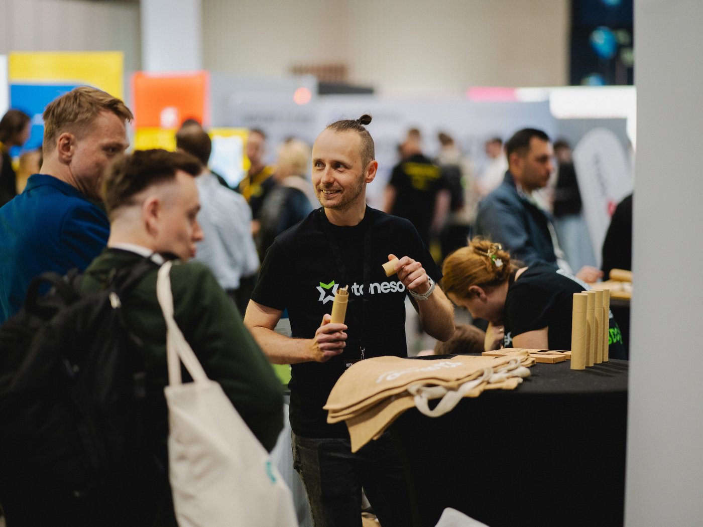 An Otoneso team member talks to visitors at the trade fair stand, holding eco-friendly paper tubes