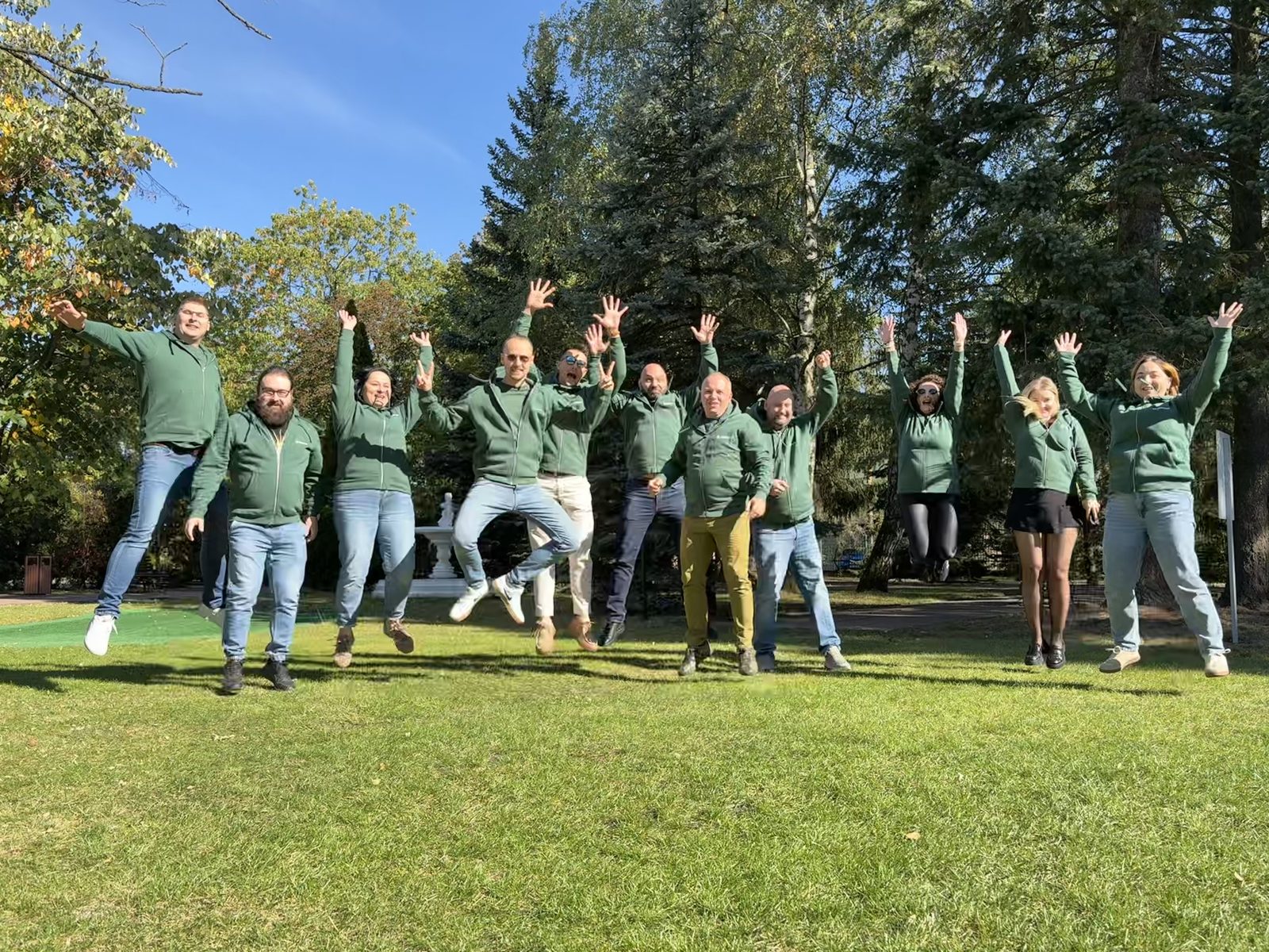 The Otoneso team in green hoodies jumping for joy on a park lawn