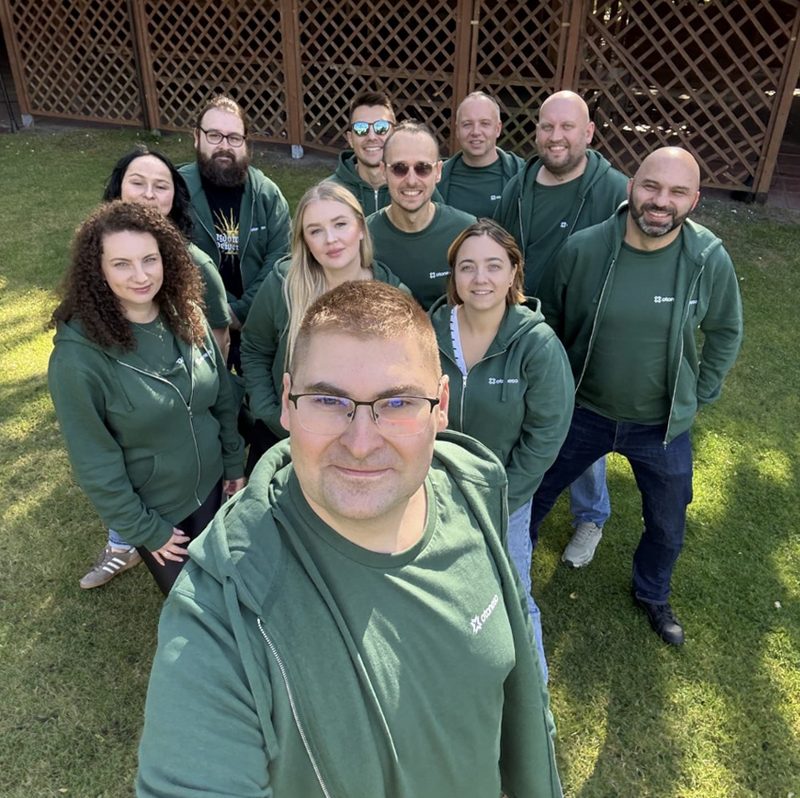 The Otoneso team, about a dozen people in green Otoneso hoodies, taking a group selfie on a lawn